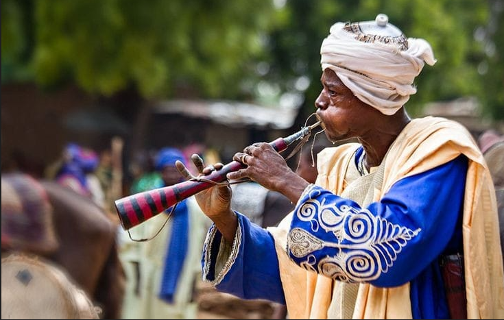 Person playing a traditional horn with a blurred background Hausa culture